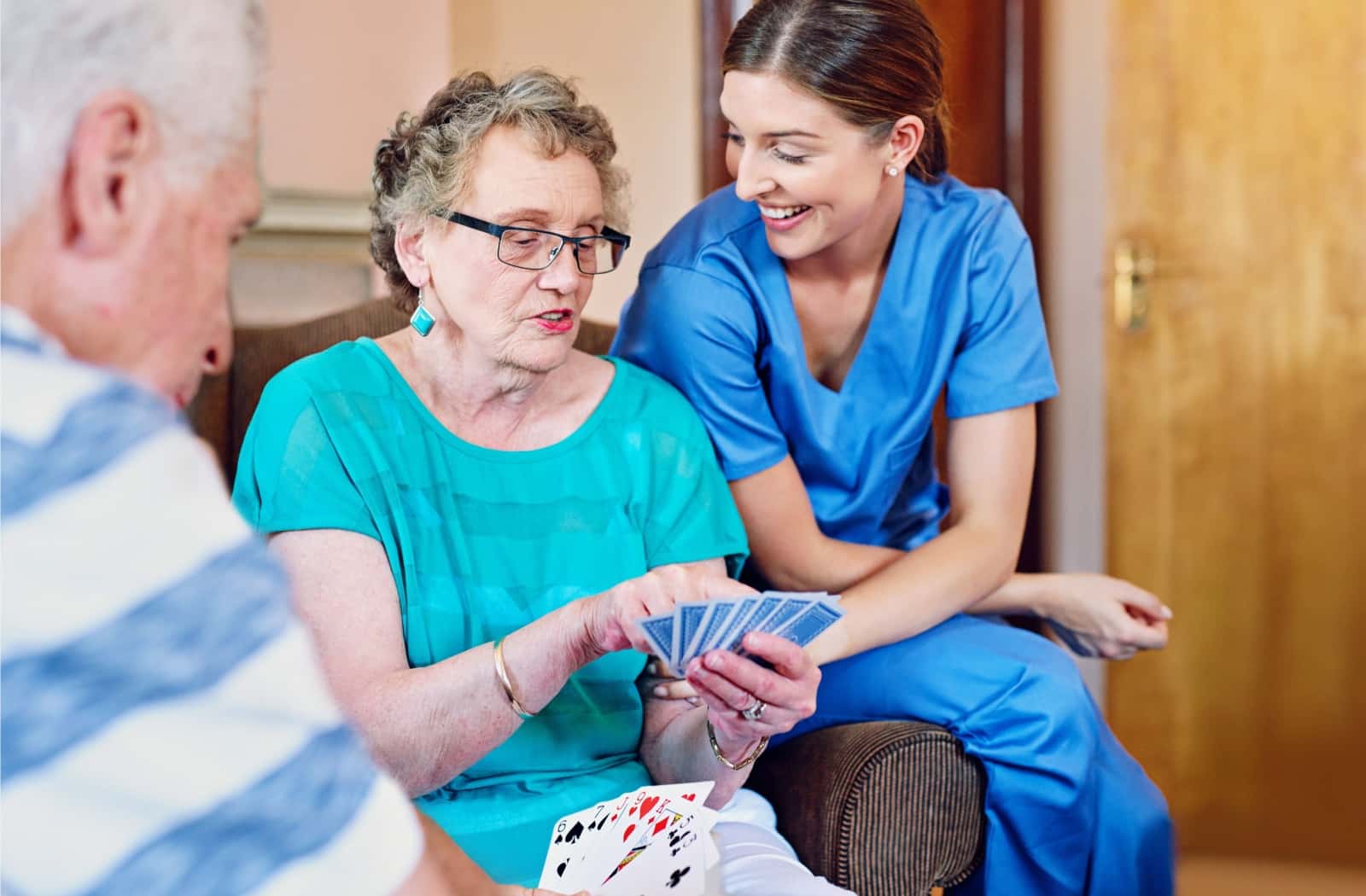 An assisted living caregiver happily supervises senior living residents playing a card game in their assisted living community.